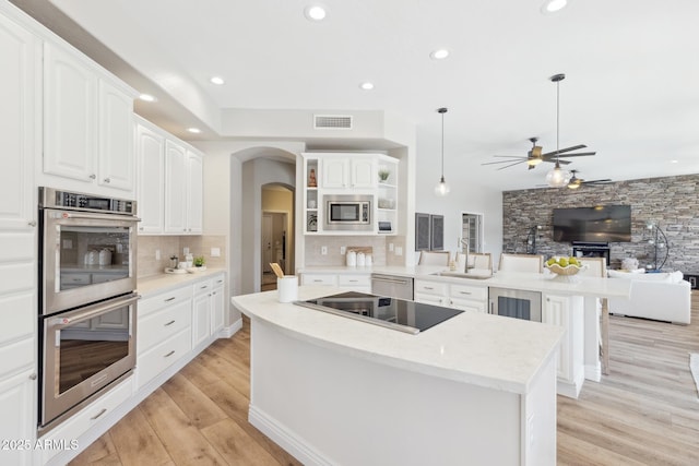 kitchen with arched walkways, decorative backsplash, appliances with stainless steel finishes, open floor plan, and a peninsula