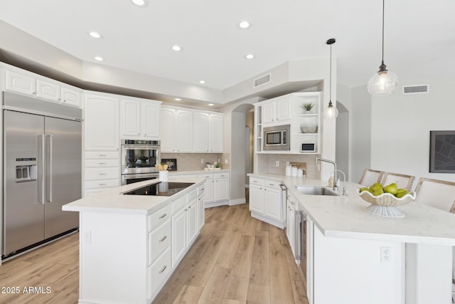 kitchen with arched walkways, open shelves, a sink, built in appliances, and a peninsula