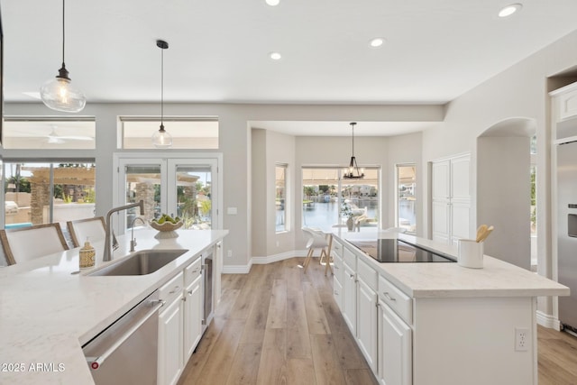 kitchen featuring light wood finished floors, white cabinets, a sink, black electric cooktop, and stainless steel dishwasher