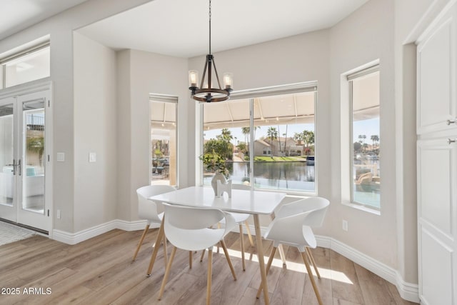 dining space with a water view, light wood finished floors, baseboards, and a notable chandelier