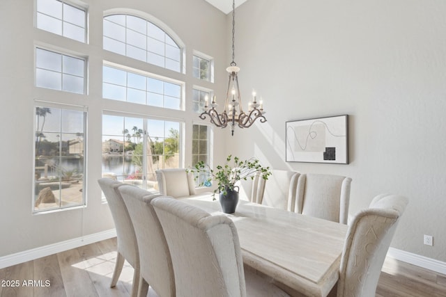 dining room featuring a notable chandelier, a water view, wood finished floors, a towering ceiling, and baseboards