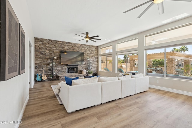 living room with plenty of natural light, ceiling fan, a fireplace, and light wood-style floors