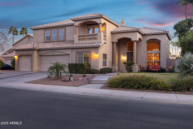 mediterranean / spanish-style home featuring a balcony, a garage, a tile roof, concrete driveway, and stucco siding