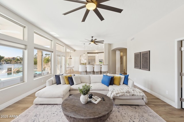 living area featuring light wood-style floors, arched walkways, visible vents, and baseboards