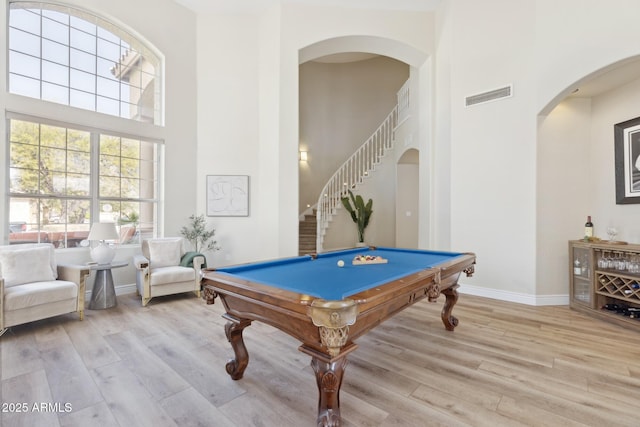 playroom with a towering ceiling, light wood-style flooring, visible vents, and arched walkways