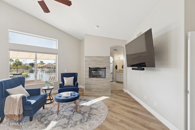 sitting room featuring ceiling fan, high vaulted ceiling, baseboards, light wood finished floors, and a tiled fireplace