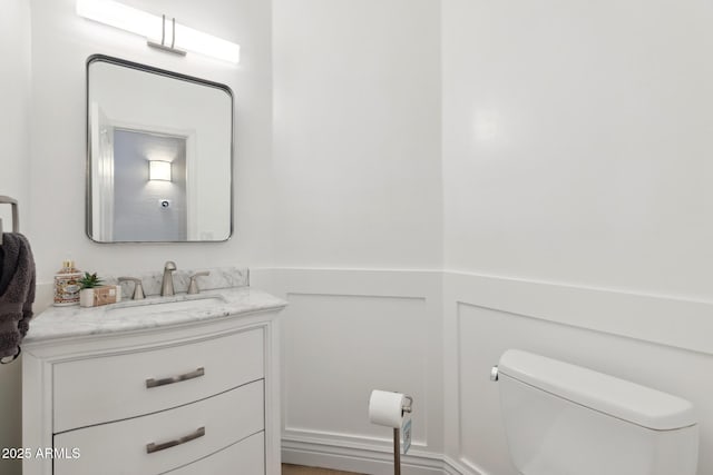 half bath with toilet, a wainscoted wall, and vanity