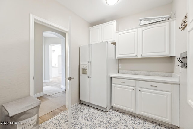 kitchen with arched walkways, white cabinetry, baseboards, light countertops, and white fridge with ice dispenser