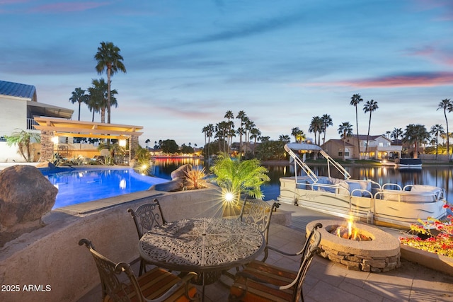 pool at dusk with a patio, an outdoor fire pit, a water view, and an outdoor pool