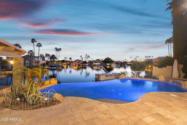 view of pool featuring a patio area, a water view, fence, and an infinity pool