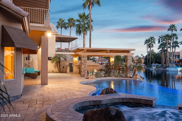 pool at dusk with an infinity pool, a patio, and an in ground hot tub