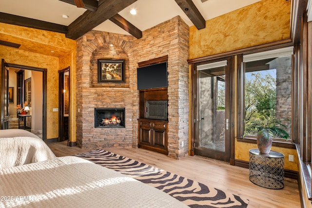 bedroom with access to exterior, an outdoor stone fireplace, beam ceiling, light wood-style flooring, and baseboards