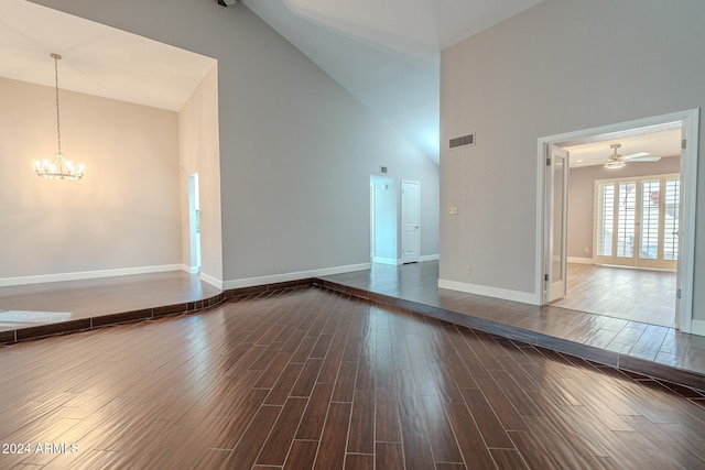 unfurnished living room with ceiling fan with notable chandelier, dark wood-type flooring, and high vaulted ceiling