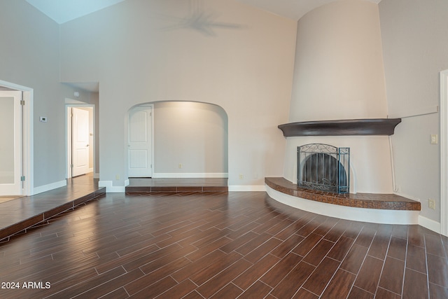 unfurnished living room with a fireplace, high vaulted ceiling, and dark wood-type flooring