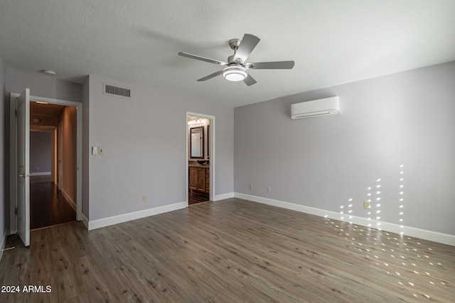 interior space featuring ensuite bath, a textured ceiling, a wall mounted AC, dark wood-type flooring, and ceiling fan