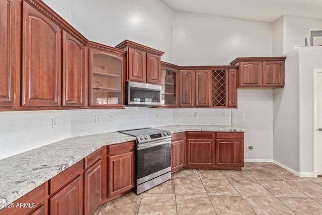 kitchen with light tile patterned floors, a towering ceiling, stainless steel appliances, and light stone counters