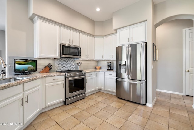 kitchen featuring decorative backsplash, light stone counters, stainless steel appliances, white cabinetry, and a sink