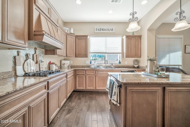 kitchen featuring stainless steel gas stovetop, a center island, hanging light fixtures, and custom range hood