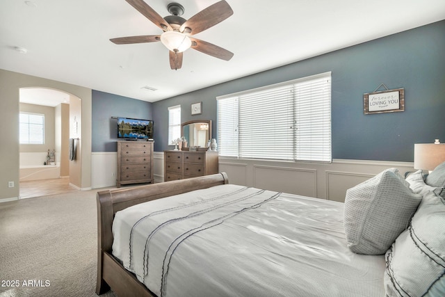 bedroom featuring ceiling fan, light colored carpet, and connected bathroom