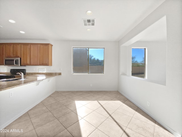 kitchen with black range, light stone countertops, light tile patterned floors, and a healthy amount of sunlight