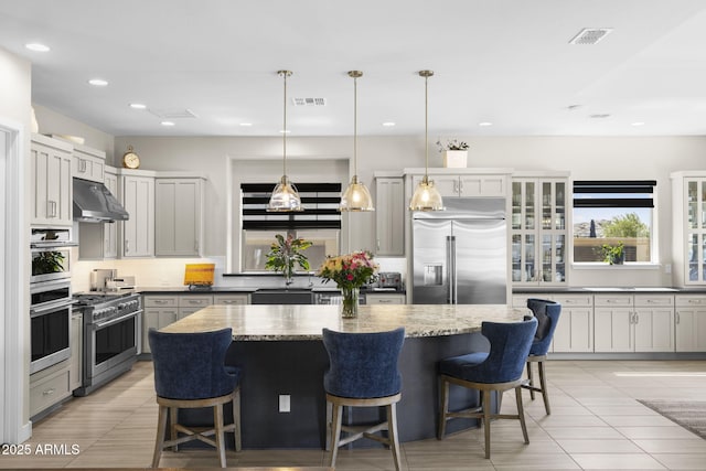 20795 W San Juan Ave, Buckeye, AZ 85396 - kitchen featuring high end appliances, under cabinet range hood, a center island, light stone counters, and backsplash