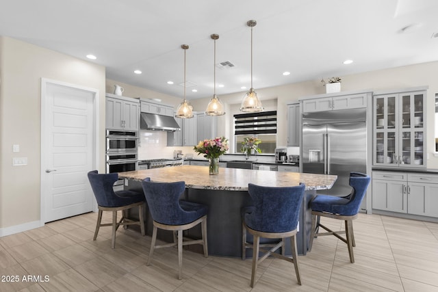20795 W San Juan Ave, Buckeye, AZ 85396 - kitchen featuring appliances with stainless steel finishes, under cabinet range hood, a kitchen island, tasteful backsplash, and light stone counters