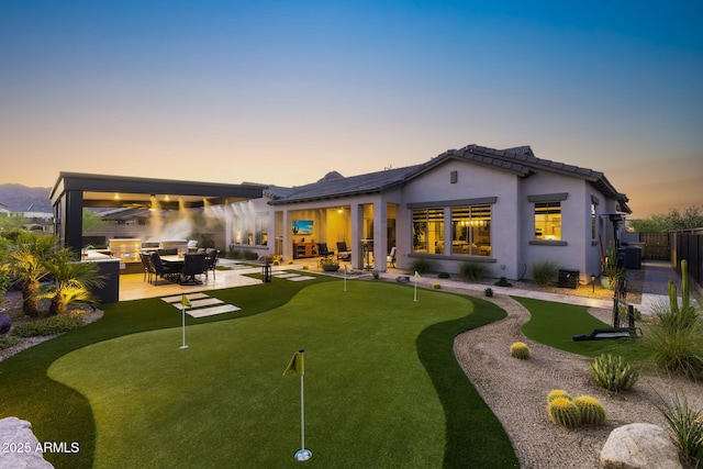 20795 W San Juan Ave, Buckeye, AZ 85396 - back of property at dusk with an area to practice putting, a patio, a fenced backyard, exterior kitchen, and stucco siding