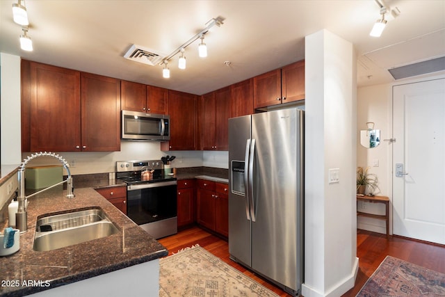 kitchen featuring dark hardwood / wood-style flooring, sink, stainless steel appliances, and dark stone counters