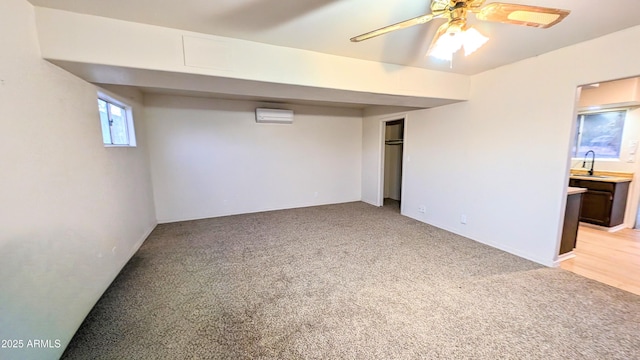 basement featuring sink, ceiling fan, a wall mounted air conditioner, and light colored carpet