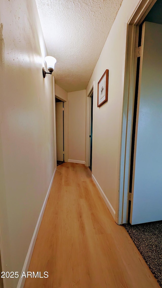 corridor with a textured ceiling and light hardwood / wood-style flooring