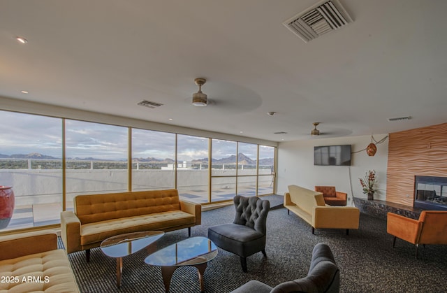 carpeted living area featuring a wall of windows, visible vents, and ceiling fan