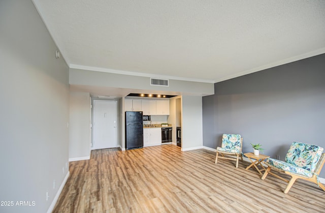 unfurnished room with light wood finished floors, visible vents, crown molding, baseboards, and a textured ceiling