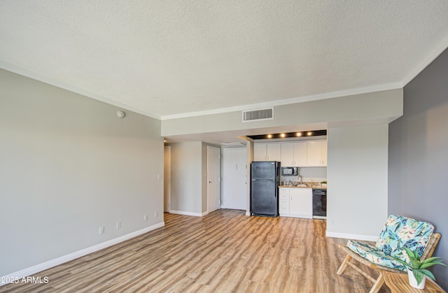 unfurnished living room with light wood finished floors, visible vents, baseboards, a textured ceiling, and a sink