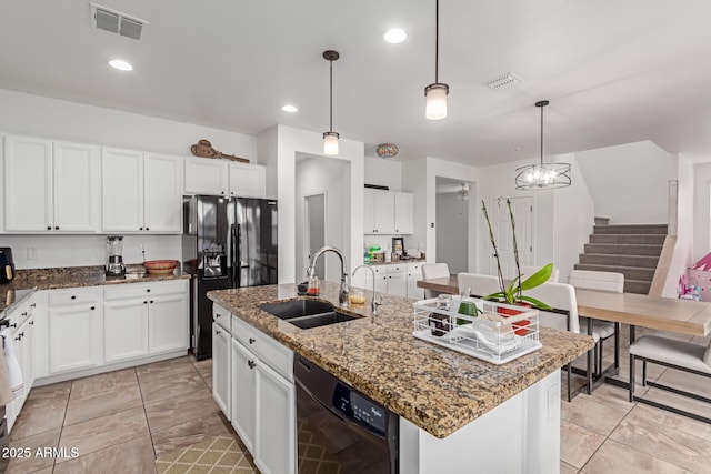 kitchen with sink, hanging light fixtures, black appliances, an island with sink, and dark stone counters