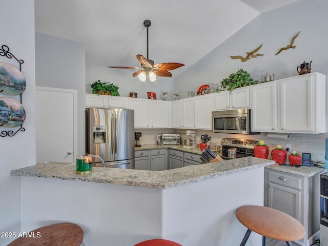 kitchen featuring appliances with stainless steel finishes, white cabinets, a kitchen bar, and kitchen peninsula