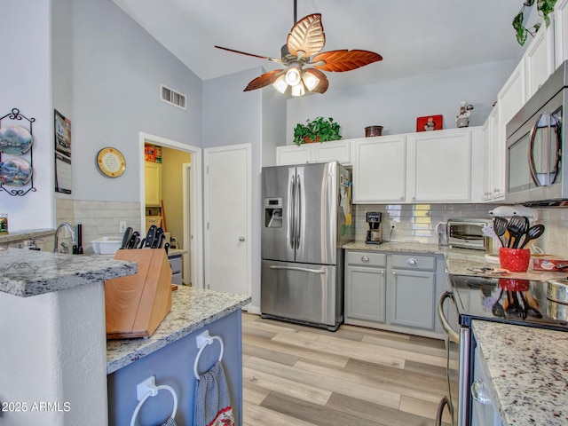 kitchen with ceiling fan, appliances with stainless steel finishes, white cabinetry, backsplash, and light wood-type flooring