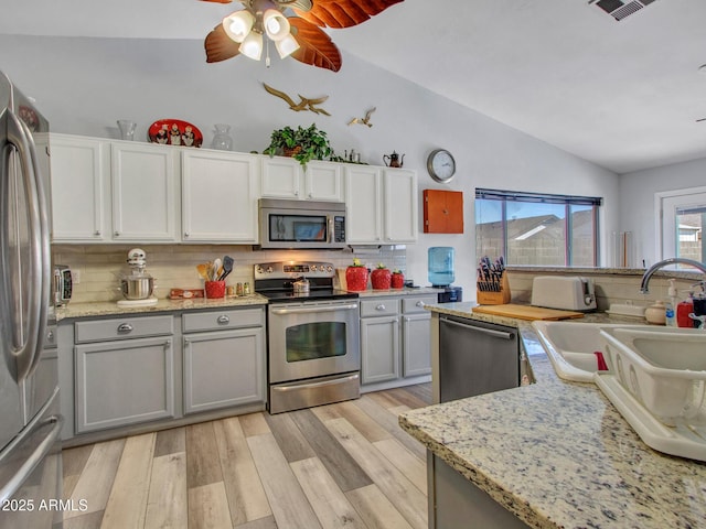 kitchen featuring sink, appliances with stainless steel finishes, light hardwood / wood-style floors, decorative backsplash, and vaulted ceiling