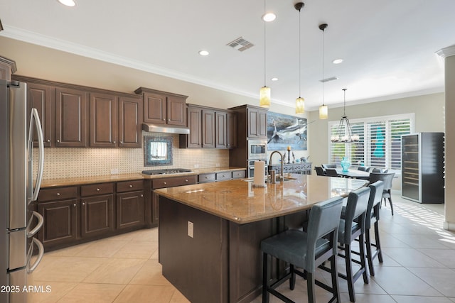 kitchen featuring visible vents, an island with sink, light stone counters, decorative light fixtures, and stainless steel appliances