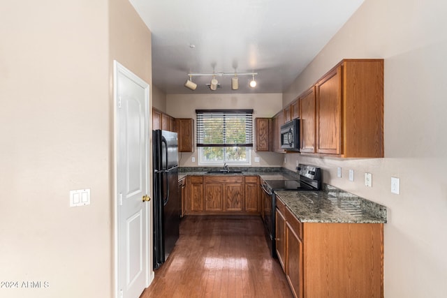 kitchen with sink, rail lighting, dark hardwood / wood-style floors, dark stone countertops, and black appliances