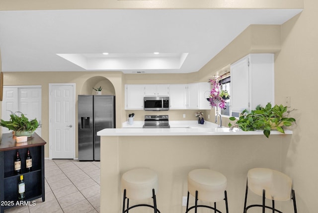 kitchen with a breakfast bar area, white cabinetry, a tray ceiling, kitchen peninsula, and stainless steel appliances