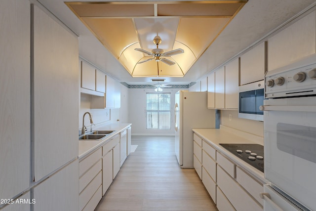 kitchen with white appliances, a tray ceiling, ceiling fan, sink, and white cabinets