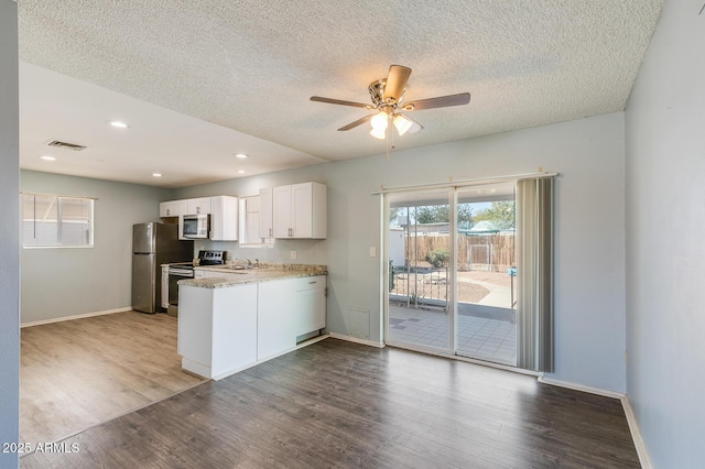 kitchen with dark wood finished floors, visible vents, appliances with stainless steel finishes, white cabinets, and a peninsula