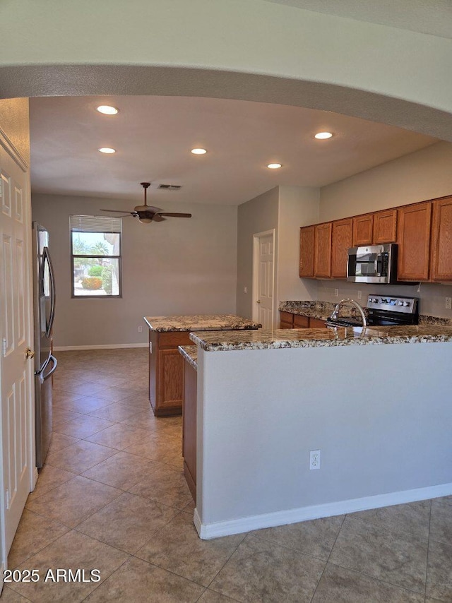 14621 W Catalina Dr, Goodyear, AZ 85395 - kitchen featuring stainless steel appliances, brown cabinetry, a ceiling fan, stone counters, and recessed lighting