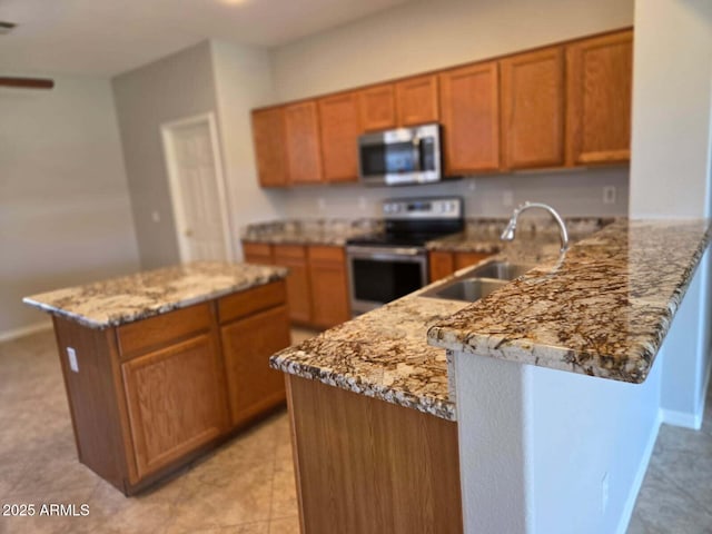 14621 W Catalina Dr, Goodyear, AZ 85395 - kitchen with appliances with stainless steel finishes, brown cabinets, light stone countertops, a peninsula, and a center island