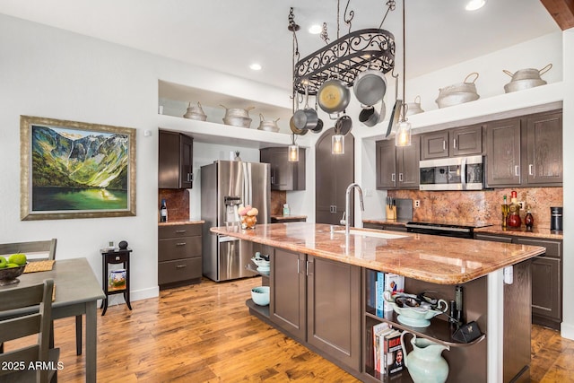 kitchen featuring open shelves, stainless steel appliances, hanging light fixtures, a kitchen island with sink, and dark brown cabinets