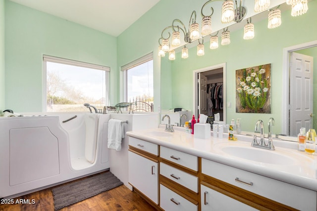 full bath with double vanity, a spacious closet, a sink, and wood finished floors