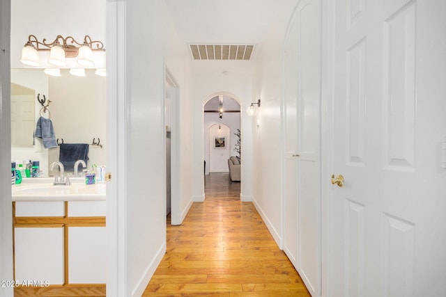 hallway featuring arched walkways, a sink, visible vents, baseboards, and light wood-type flooring