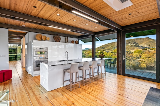 kitchen with wooden ceiling, a sink, light wood-type flooring, double oven, and beam ceiling