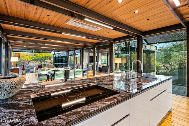 kitchen featuring sink, dark stone countertops, black cooktop, white cabinetry, and a wall of windows