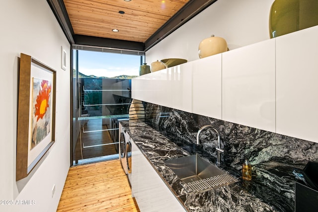 kitchen with white cabinetry, sink, wooden ceiling, dark stone countertops, and light hardwood / wood-style floors